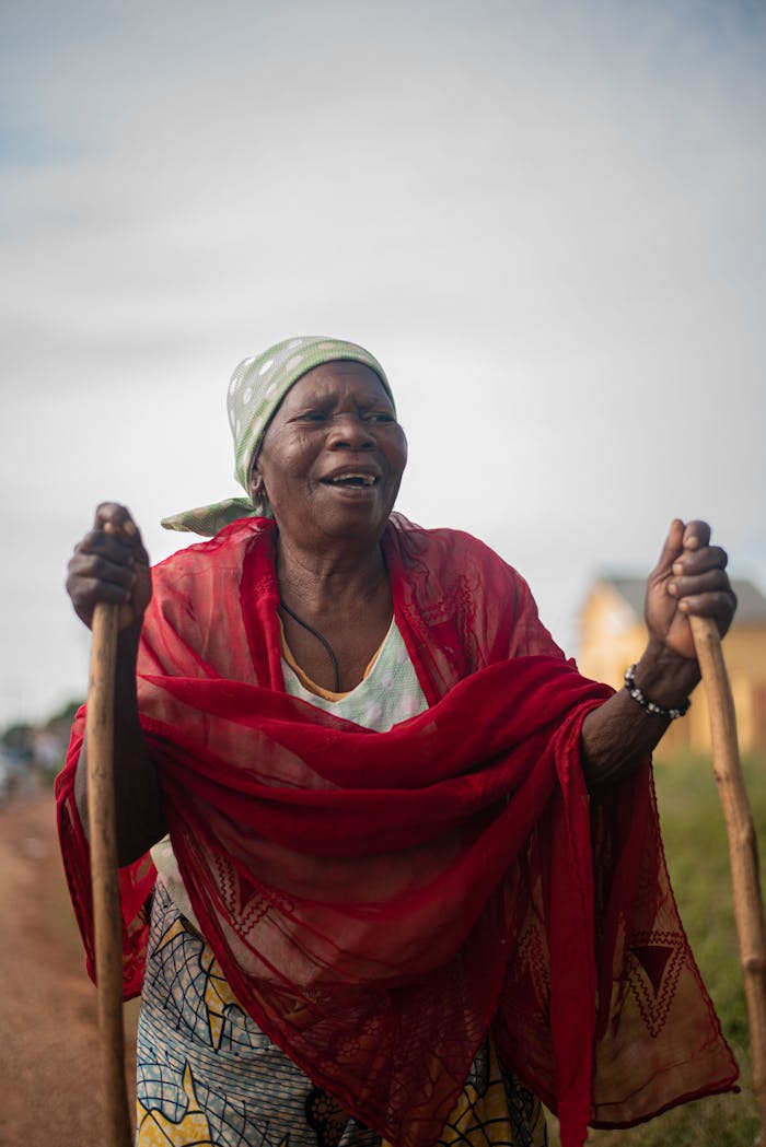 Elderly woman joyfully walking with support of sticks outdoors in a rural area.